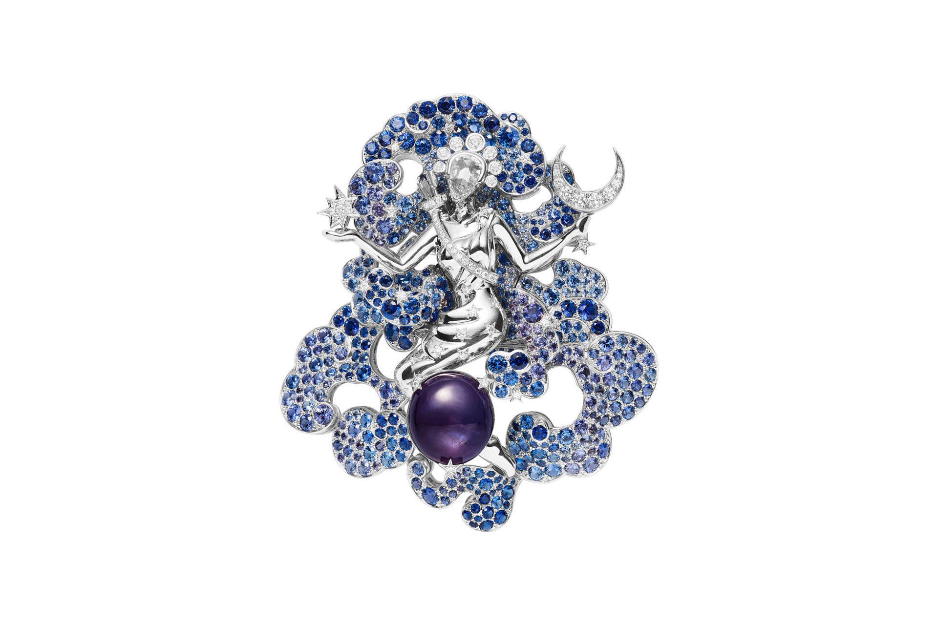 A jeweled brooch featuring a silver female figure holding a star and crescent moon, surrounded by blue gemstones and a large purple gemstone at the bottom, set against a white background.