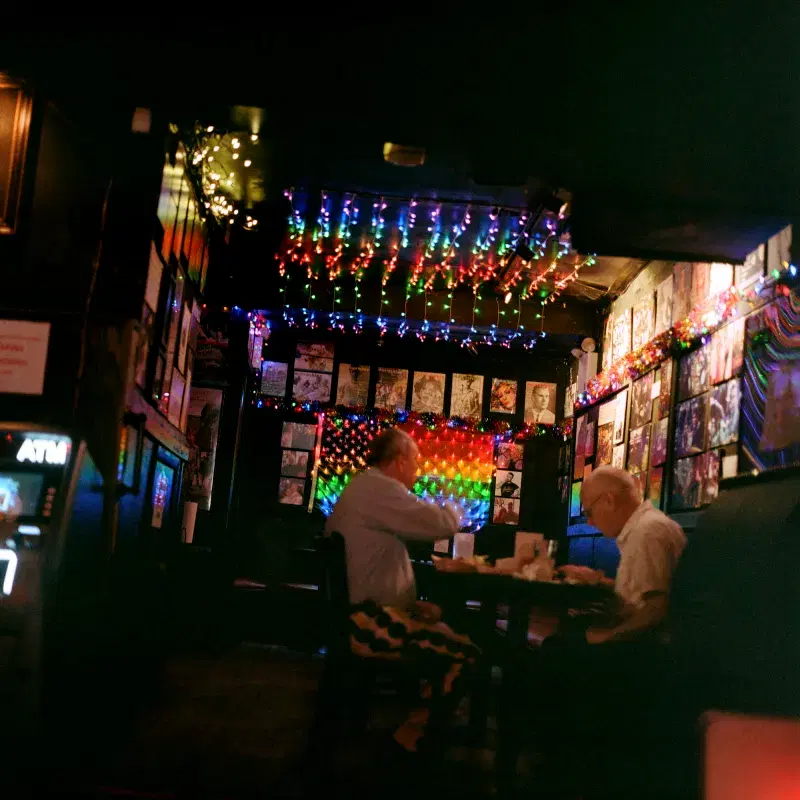 People having drinks and food inside Bar with colored lights hanging from the ceiling 