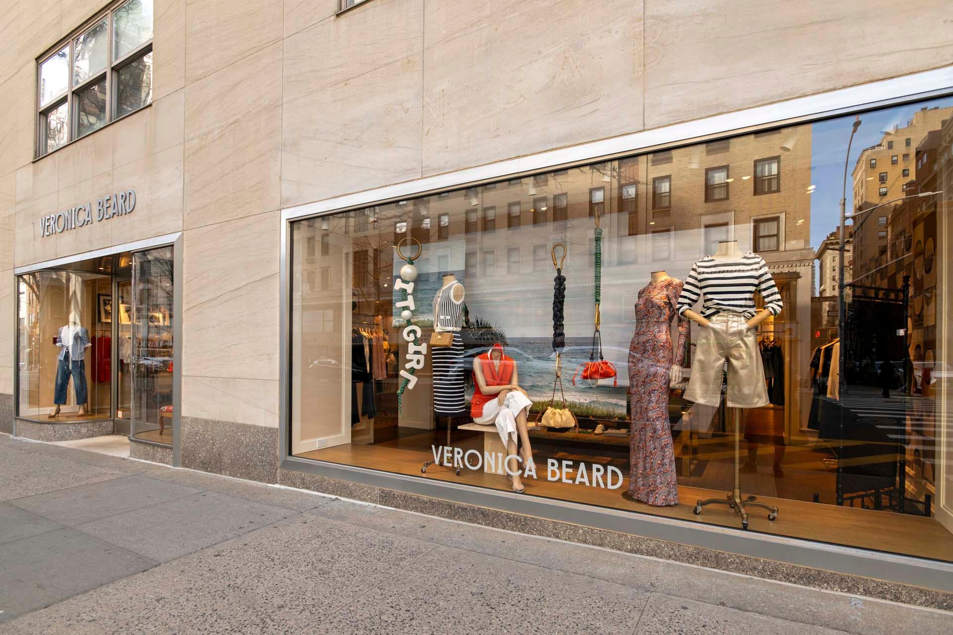 A large storefront window displays mannequins wearing fashionable clothing, including striped tops and a dress. Inside, the store is visible with more clothing. The shop's name, Veronica Beard, is displayed above the window.