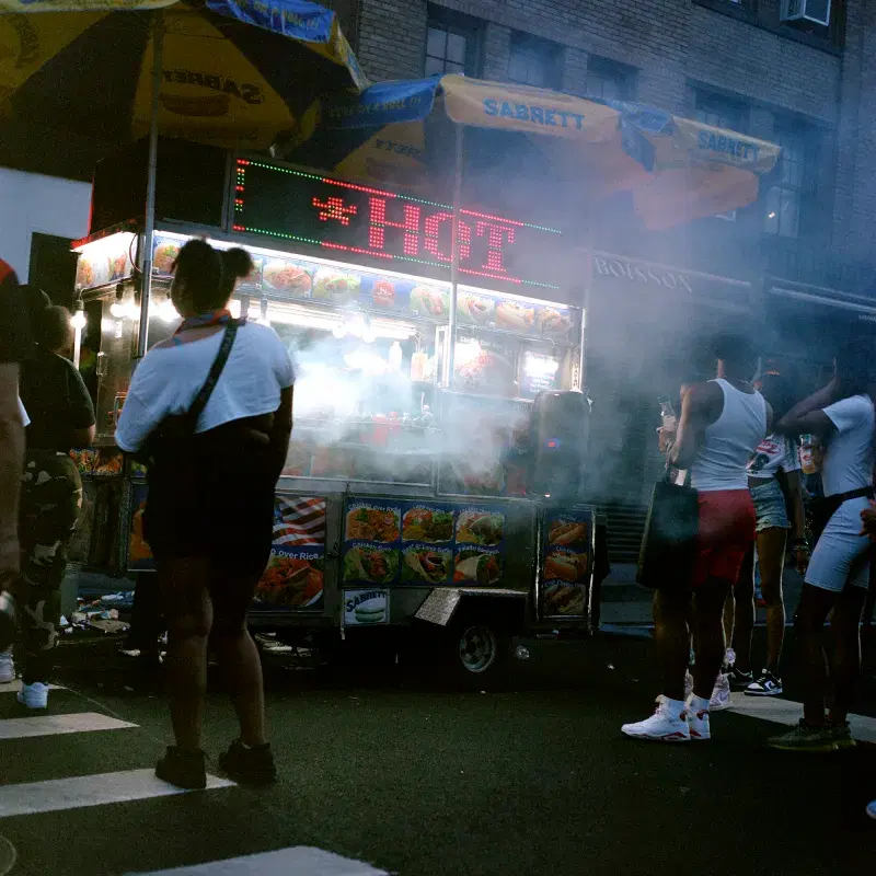 People walking around hot dog stand