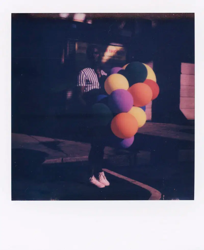Polaroid picture of person holding colorful balloons on the street