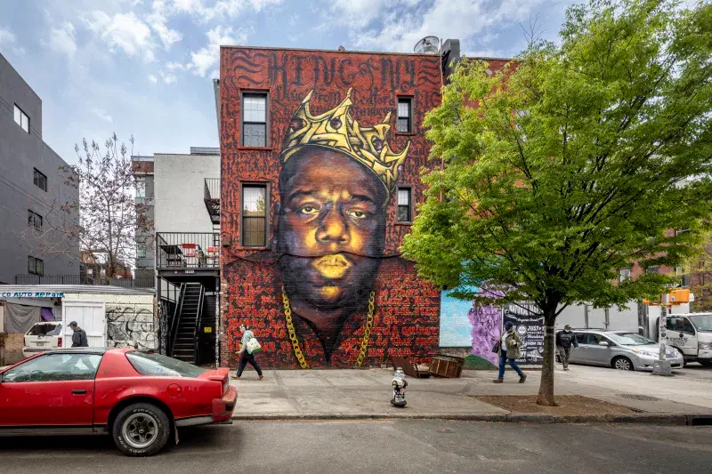 Mural of Notorius B.I.G wearing a gold crown and necklace on wall facing the street