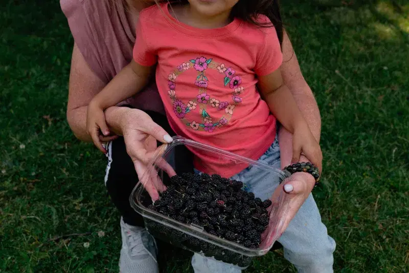 A kid and an older person holding a bowl filled with berries at Silver Lake Park in Staten Island