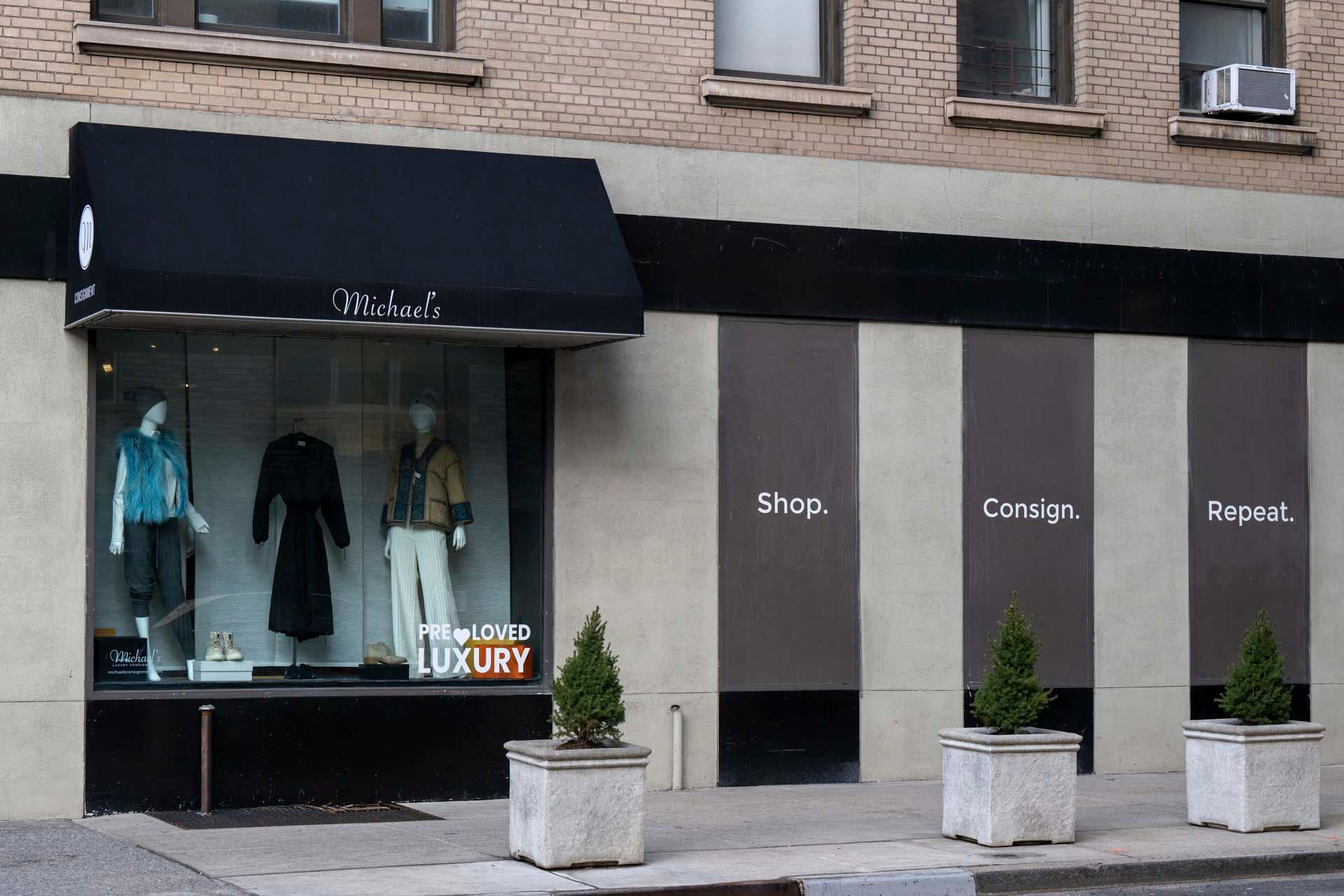 Storefront of a consignment shop with a black awning displaying mannequins dressed in stylish outfits. The window reads "Pre-Loved Luxury." The wall has the text "Shop. Consign. Repeat." Two potted plants flank the entry.
