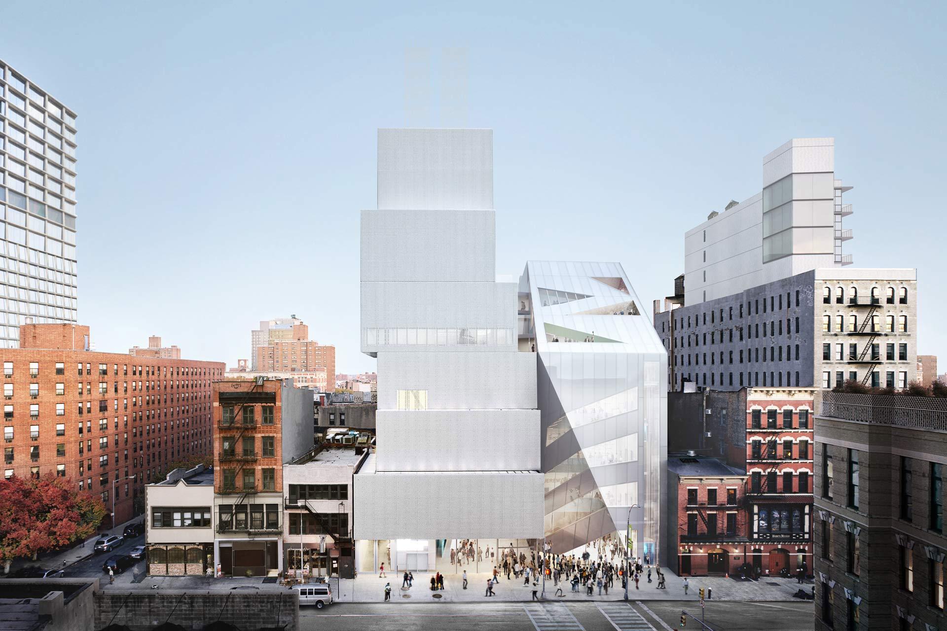 A modern, multi-level building with stacked, box-like structures and angular glass facades stands out among older brick buildings on a city street with people gathered at its base.