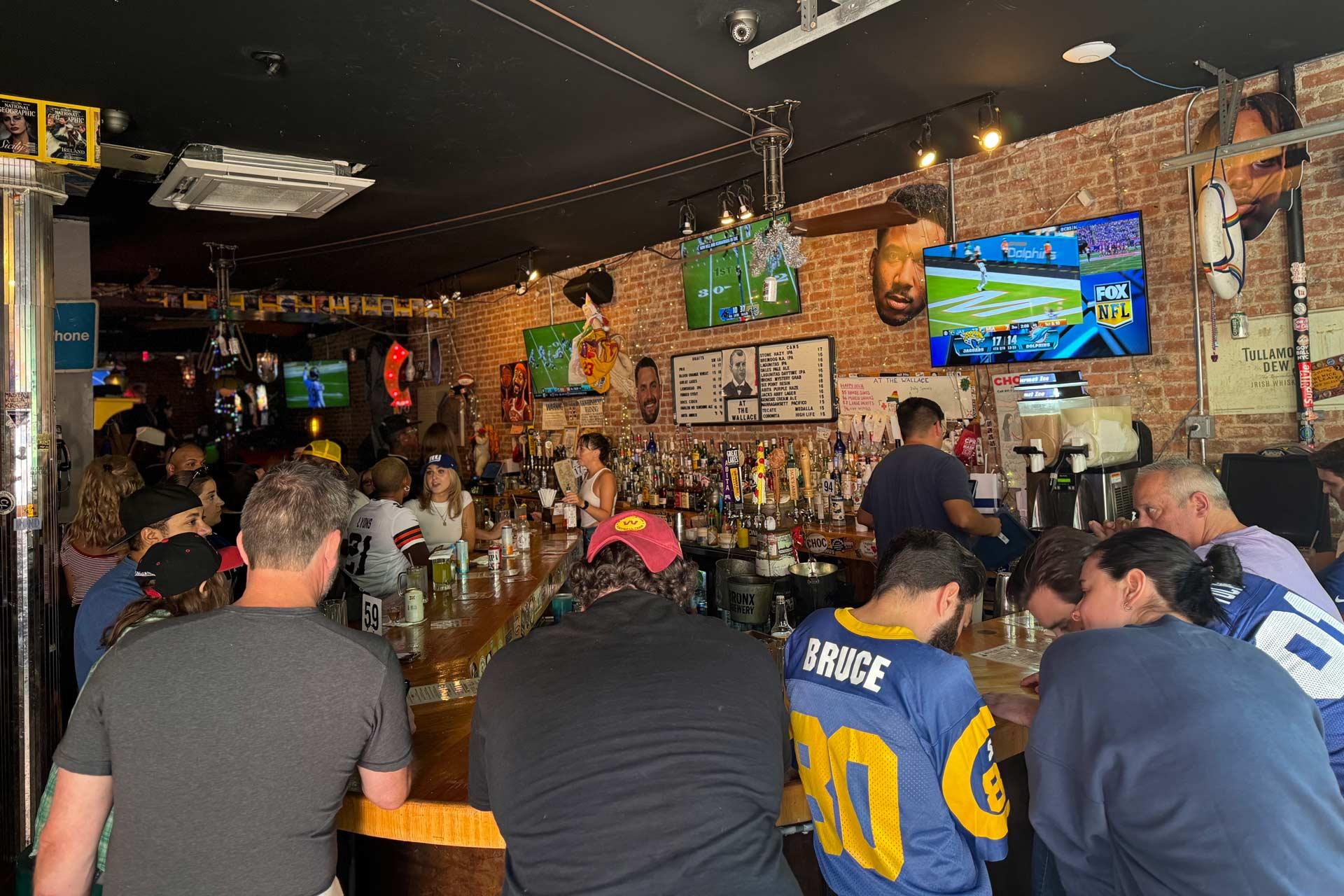 Patrons sit at a bar lined with sports memorabilia and televisions broadcasting football games.