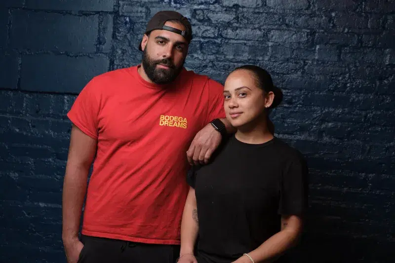 Portrait of Jeremy Batista and Angela Espinal posing in front of a brick wall