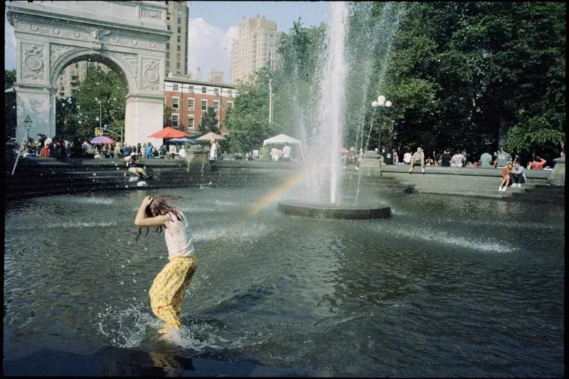 A kid inside the fountain at Washington Square Park in Manhattan, a rainbow in the background