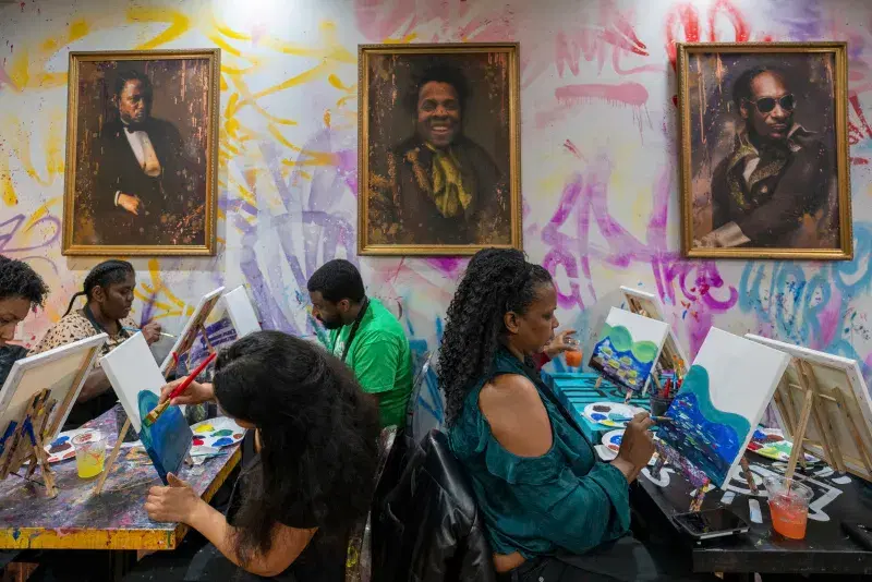 a group of people painting around a table with paintings on the wall.